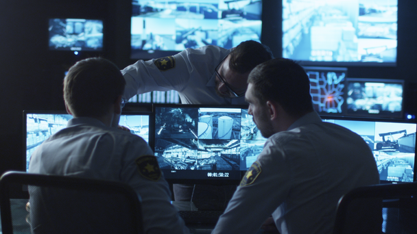 Gruppe von Sicherheitsbeamten unterhält sich bei der Arbeit in einem dunklen Überwachungsraum mit Bildschirmen. - Filmmaterial, Video