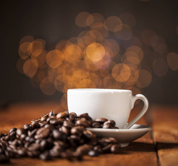 Šálek kávy a kávových zrn na dřevěný stůl a bokeh pozadí - Fotografie, Obrázek