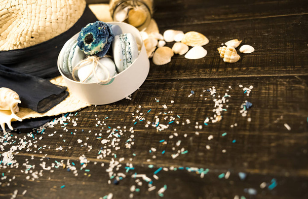 Sombrero de paja con macarrones azules y sal marina con conchas en el fondo de madera
 - Foto, Imagen