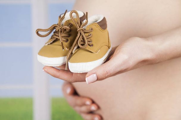 беременная женщина держит детские туфли  - Фото, изображение