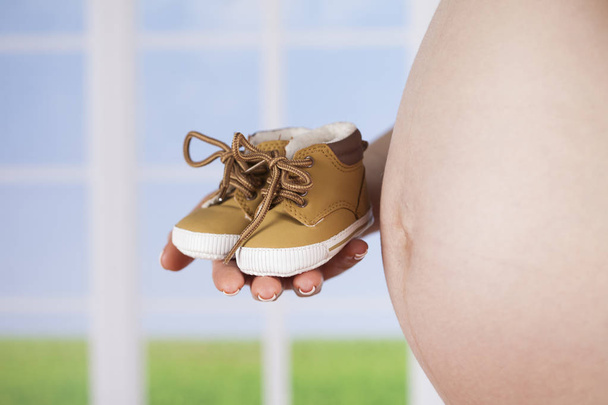 mujer embarazada sosteniendo zapatos de bebé  - Foto, imagen