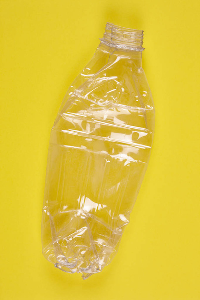 Дробленая пластиковая бутылка с желтым фоном. Переработанный мусор
 - Фото, изображение