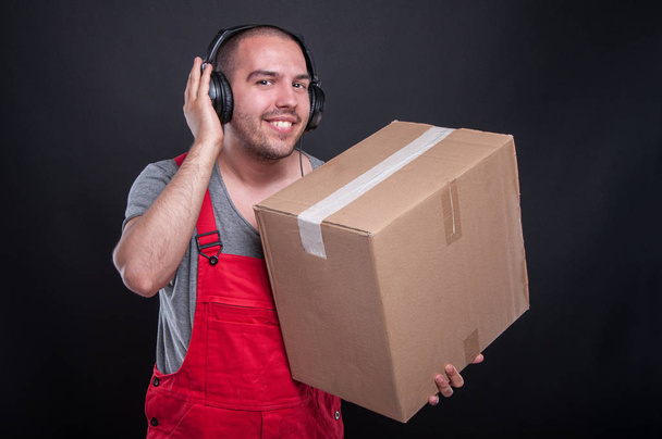 Парень-носитель улыбается, держа коробку и слушая гарнитуру
 - Фото, изображение