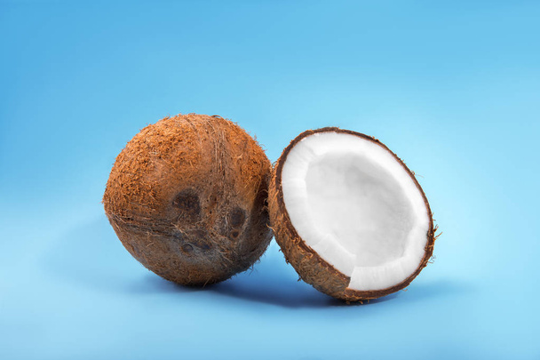 A pair of organic coconuts on a blue background. A coconut cracked in half and a whole nut. Healthy summer fruits.  - Valokuva, kuva
