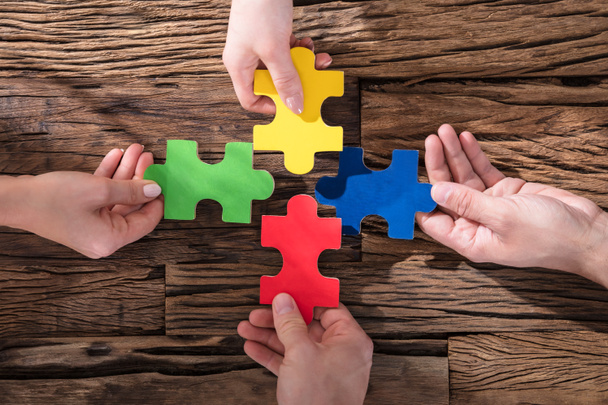 Elevated View Of Hands Holding Colorful Jigsaw Puzzle On Wooden Desk - Foto, Bild
