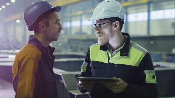Mérnök és a munkavállaló a hardhats, amelyek a beszélgetés a nehézipar gyár. - Felvétel, videó