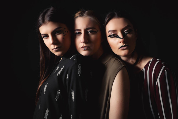 Три стильні моделі з незвичайним макіяжем та рисами обличчя на темному тлі
 - Фото, зображення