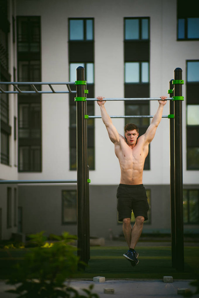 Handsome sexy male bodybuilder athlete man doing crossfit workout in athletic facilities on sunny morning outdoors. Healthy lifestyle concept. Physical preparation of body. pull-up on horizontal bar - Φωτογραφία, εικόνα