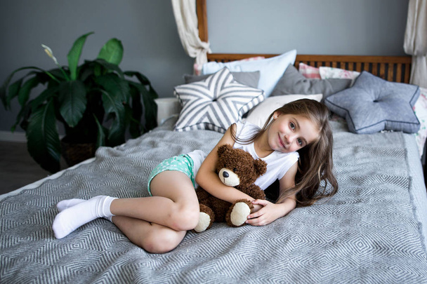 Roztomilá holčička hraje s hračka medvěd na posteli - Fotografie, Obrázek