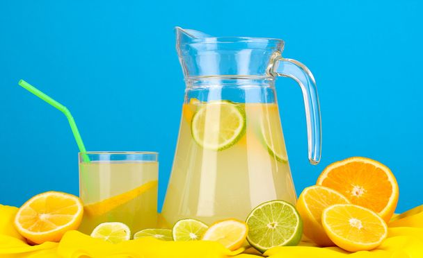Цитрусовий лимонад в склі і глечик цитрусових навколо на жовтій тканині на синьому фоні
 - Фото, зображення