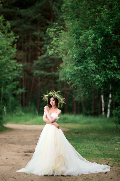 Beautiful bride in a white dress with a wreath of flowers - Fotó, kép