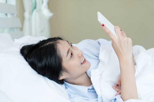 Gyönyörű ázsiai tinédzser nő fehér ágyban fekve, és használ egy p - Fotó, kép