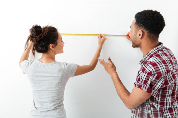 Happy young couple standing and using measuring tape - Фото, изображение