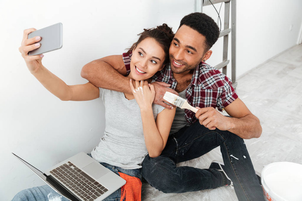 Cheerful young loving couple sitting on floor make selfie - Photo, image