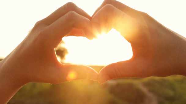 Ellerini iç batan güneşin ışınları ile kalp şeklinde silüeti - Video, Çekim