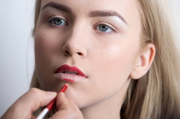 Girl getting red pencil on lips by male hand - Foto, Bild