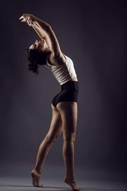 Portret piękna szczupła dziewczyna sportowca z fryzury updo boso taniec pod studio reflektorzy sobie biały top i majtki czarny wysokiej talii - Zdjęcie, obraz