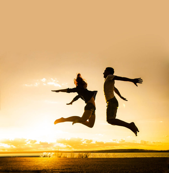 family  on the beach.  Silhouette of a couple - man and woman jumping on the beach on sunset background  - Foto, afbeelding