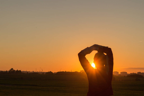 силует заднього виду молодої жінки, що стоїть з руками за головою і дивиться на захід сонця
 - Фото, зображення