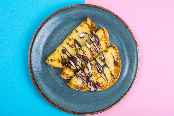 Sweet pancakes with chocolate topping on pastel background - Fotó, kép