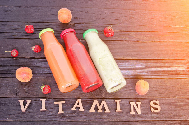 drei Flaschen mit Saft, Obst und Inschrift Vitamine auf hölzernem Hintergrund, Lebensmittelkonzept - Foto, Bild