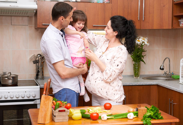счастливая семья с ребенком в интерьере домашней кухни со свежими фруктами и овощами, беременная женщина, концепция здорового питания
 - Фото, изображение