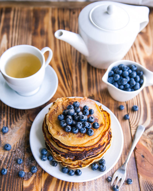 Crêpes petit déjeuner sain avec des bleuets, whortleberry tourbière, tasse de thé vert, tasse de bleuets et théière sur fond de bois brun
  - Photo, image