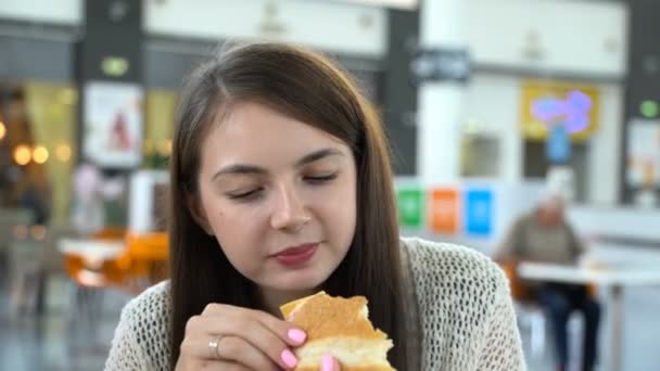Het meisje is het eten van een hamburger op een food court. - Video