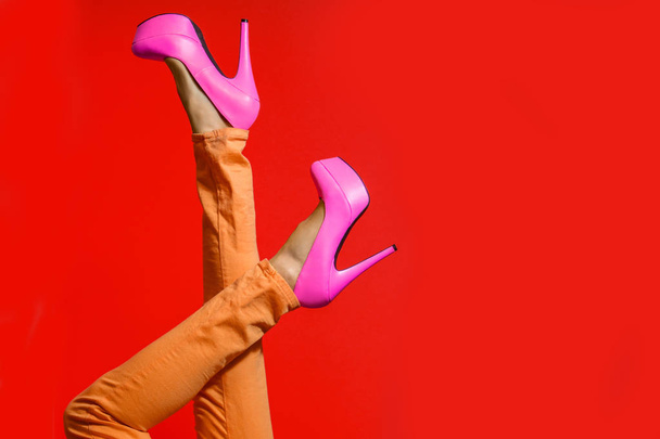 Female legs wearing high heels over bright red background - 写真・画像
