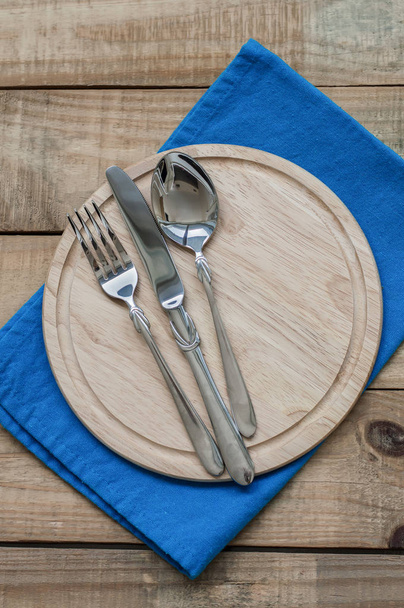 Mutfak sofra dikey fotoğraf: bıçak, çatal ve kaşık ile mavi peçete ahşap kesme tahtası üzerinde - Fotoğraf, Görsel
