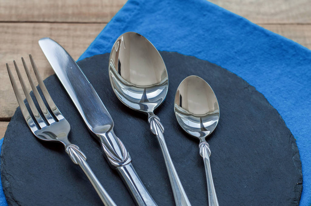 Couteau, fourchette, grandes et petites cuillères sur planche d'ardoise noire et serviette bleue
 - Photo, image