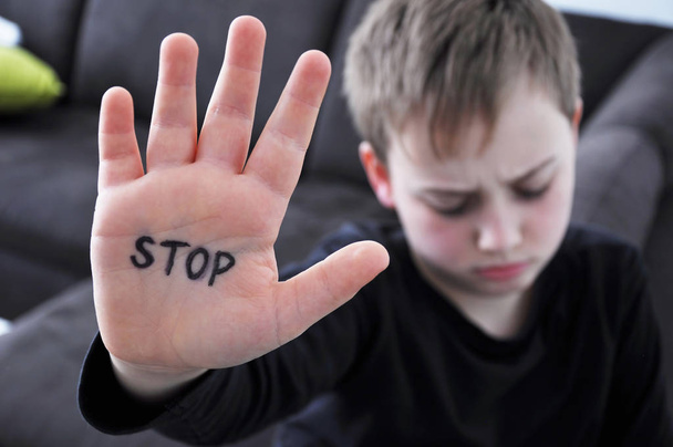 Маленький мальчик, подвергшийся насилию, держит руку со словом "СТОП", написанным на ней. Концепция домашнего насилия и жестокого обращения с детьми
. - Фото, изображение