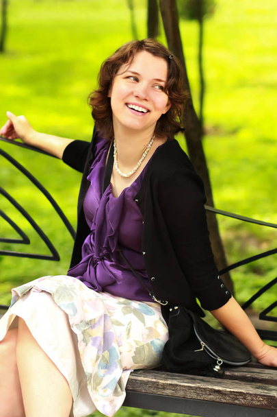Retrato de una joven feliz y sonriente sentada en el banco del parque
 - Foto, Imagen