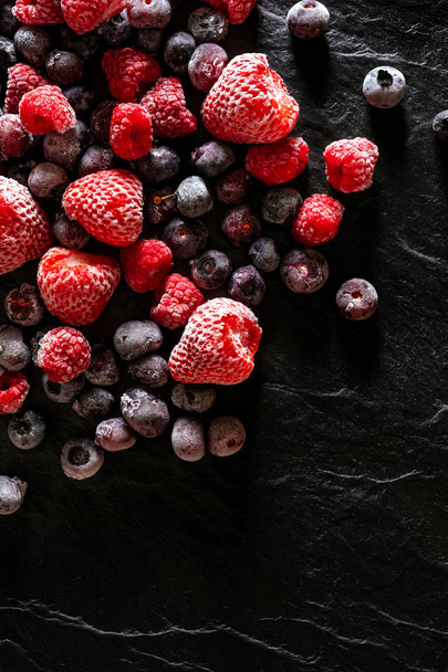 gefrorene Himbeeren, Blaubeeren und Erdbeeren auf schwarzem Steinhintergrund, Draufsicht - Foto, Bild