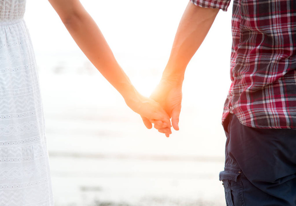 Zamilovaný mladý pár, atraktivní muž a žena si užívají romantický večer na pláži, drží se za ruce při západu slunce - Fotografie, Obrázek
