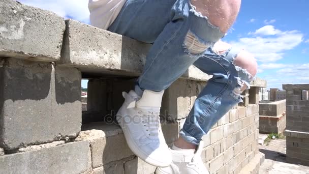 Mladá zrzka člověka v bílou mikinu sedí na cihlovou zeď na střeše - Záběry, video