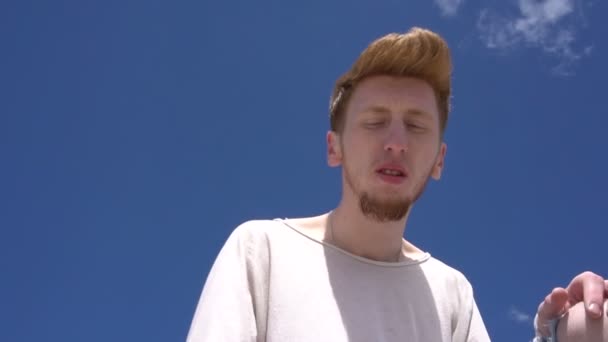 Steadicam shot of a young red haired stilish man against clear blue sky background. - Felvétel, videó