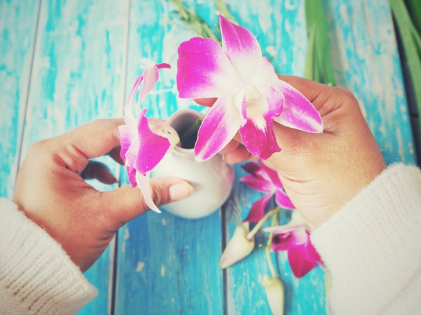 levágott kép nő, ami elrendezése rózsaszín orchideák, kék kopott asztalnál - Fotó, kép