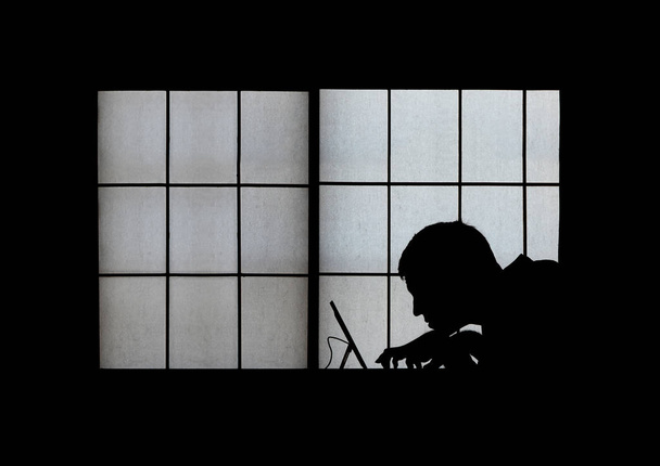 Silueta de ventana de un espeluznante pirata informático encorvado sobre una computadora portátil tarde en la noche
 - Foto, Imagen