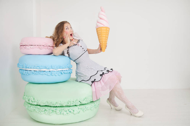 pretty young lady in polka dot pin up dress with giant sweets in white background studio - Foto, Bild