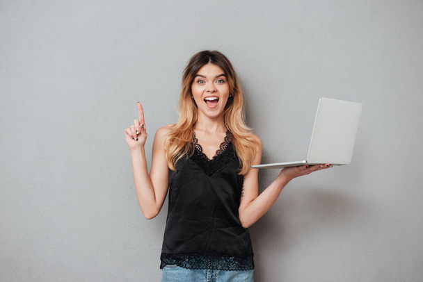 Excited girl holding laptop and pointing finger up at copyspace - Fotoğraf, Görsel