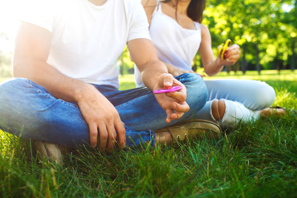 Young girl and boy playing with a fidget spinners in the park. stress relieving toy. Sunny summer day. They laugh and smile - 写真・画像