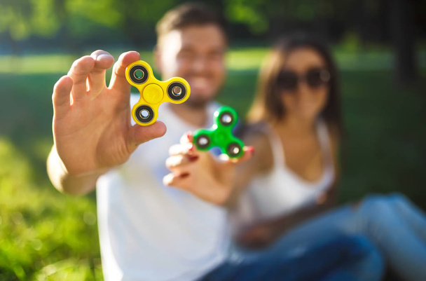 Young girl and boy playing with a fidget spinners in the park. stress relieving toy. Sunny summer day. They laugh and smile - Photo, Image