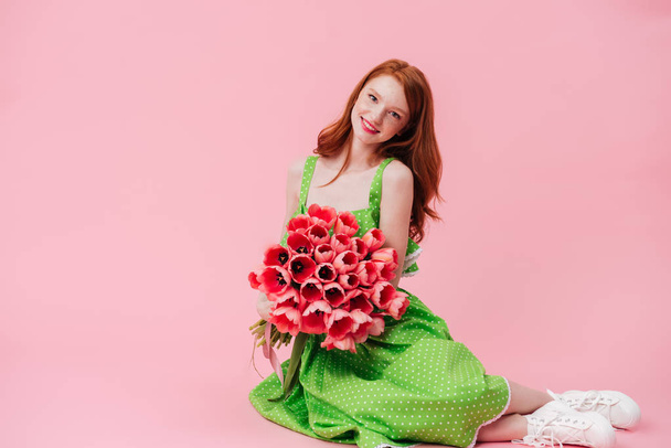 Smiling ginger woman sitting on floor with bouquet of flowers - Foto, immagini