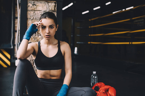 Young woman sitting on the floor after hard workout in gym. - Photo, Image