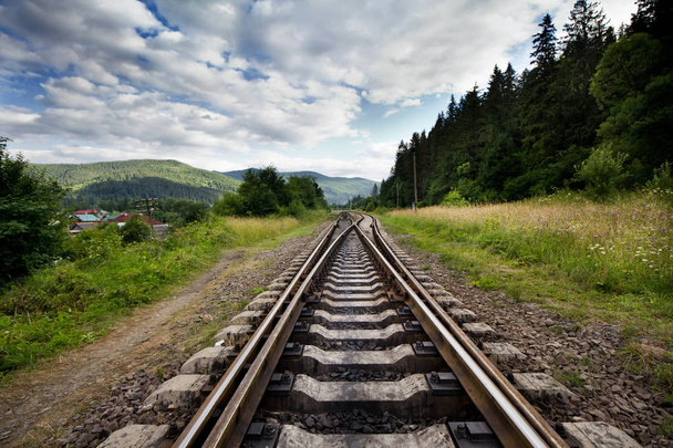 Eisenbahn gegen Berge und schönen Himmel, in der Nähe von Wald.  - Foto, Bild