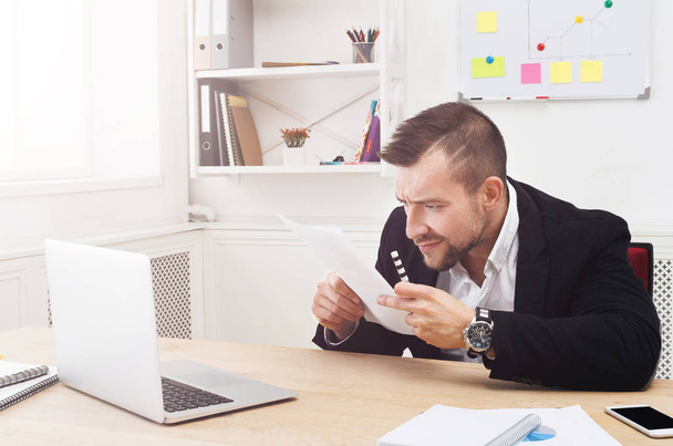 Young concentrated businessman read documents in modern white office - Foto, Imagen