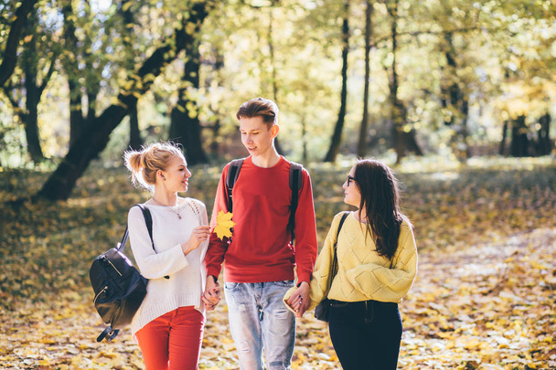 Concepto de educación, estilo de vida y personas: hombre joven con camisa roja y dos niñas caminando y hablando en el parque de otoño
. - Foto, imagen