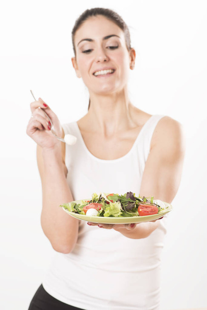 Молодая женщина ест салат и держит смешанный салат
 - Фото, изображение