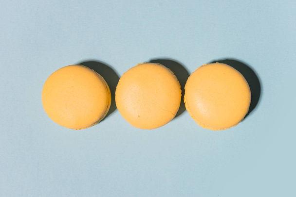 Three sweet yellow macaroons on blue table background. - Zdjęcie, obraz